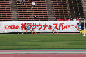 神戸サウナの横断幕の前を、アスリートたちが走っている。